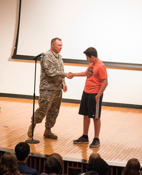 Col. Robert O'Brien shakes the hand and presents a commanders coin to a GEMS student